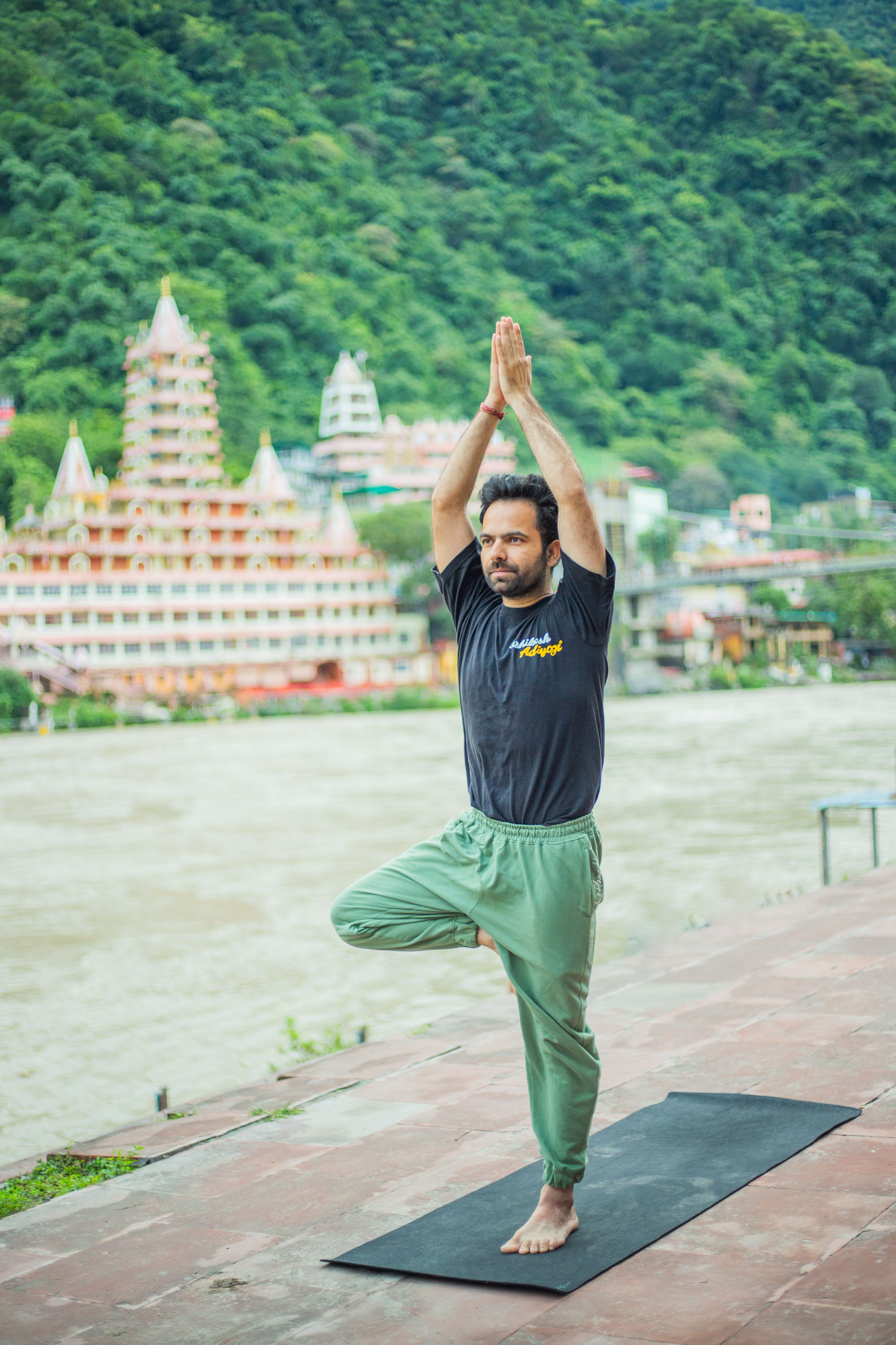 A man performing yoga on a riverside terrace in Rishikesh with temples in the background.