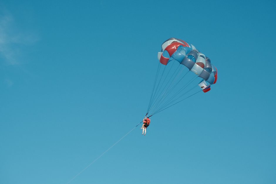 A person parasailing under a blue sky, captured in mid-flight with colorful parachute.