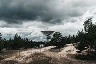 A large radio telescope in Latvia set against a backdrop of stormy skies and lush greenery.