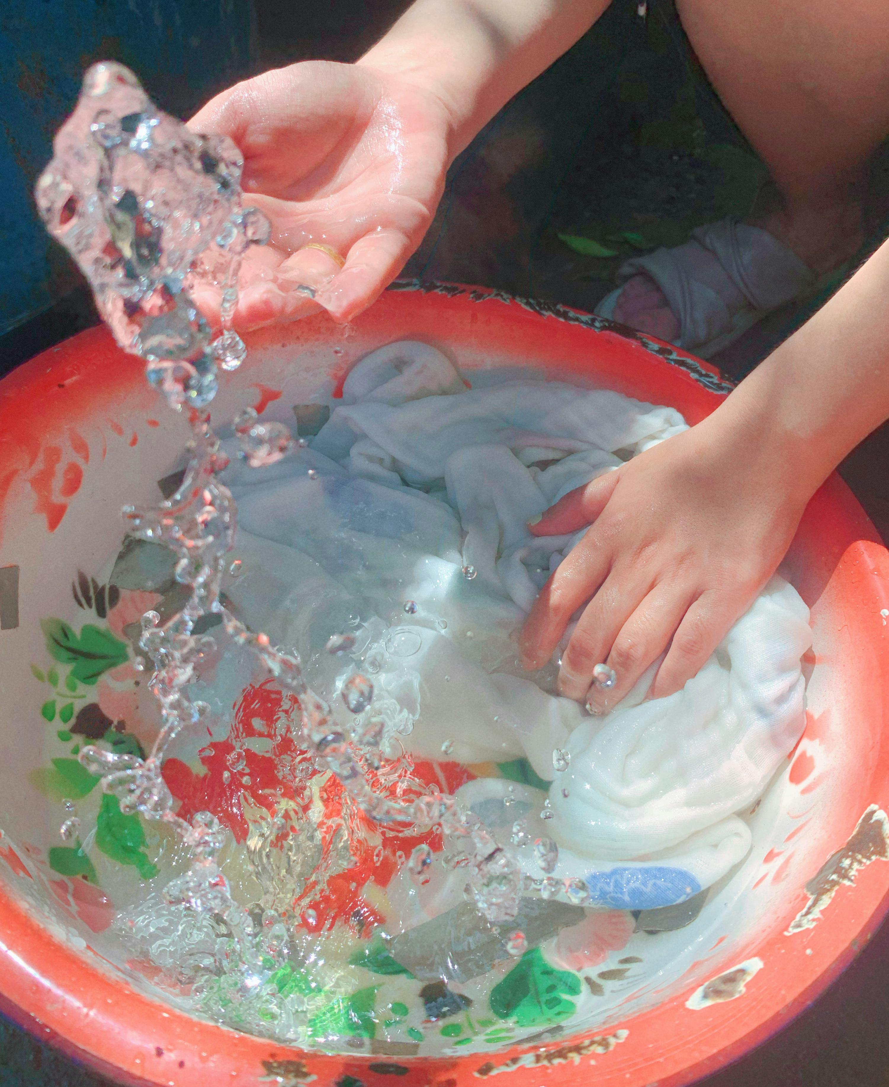 Free Close-up of hands washing clothes in a red basin outdoors. Sunny day. Stock Photo