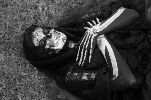 Free Person with detailed skeleton face and body paint lying on grass in black and white. Stock Photo