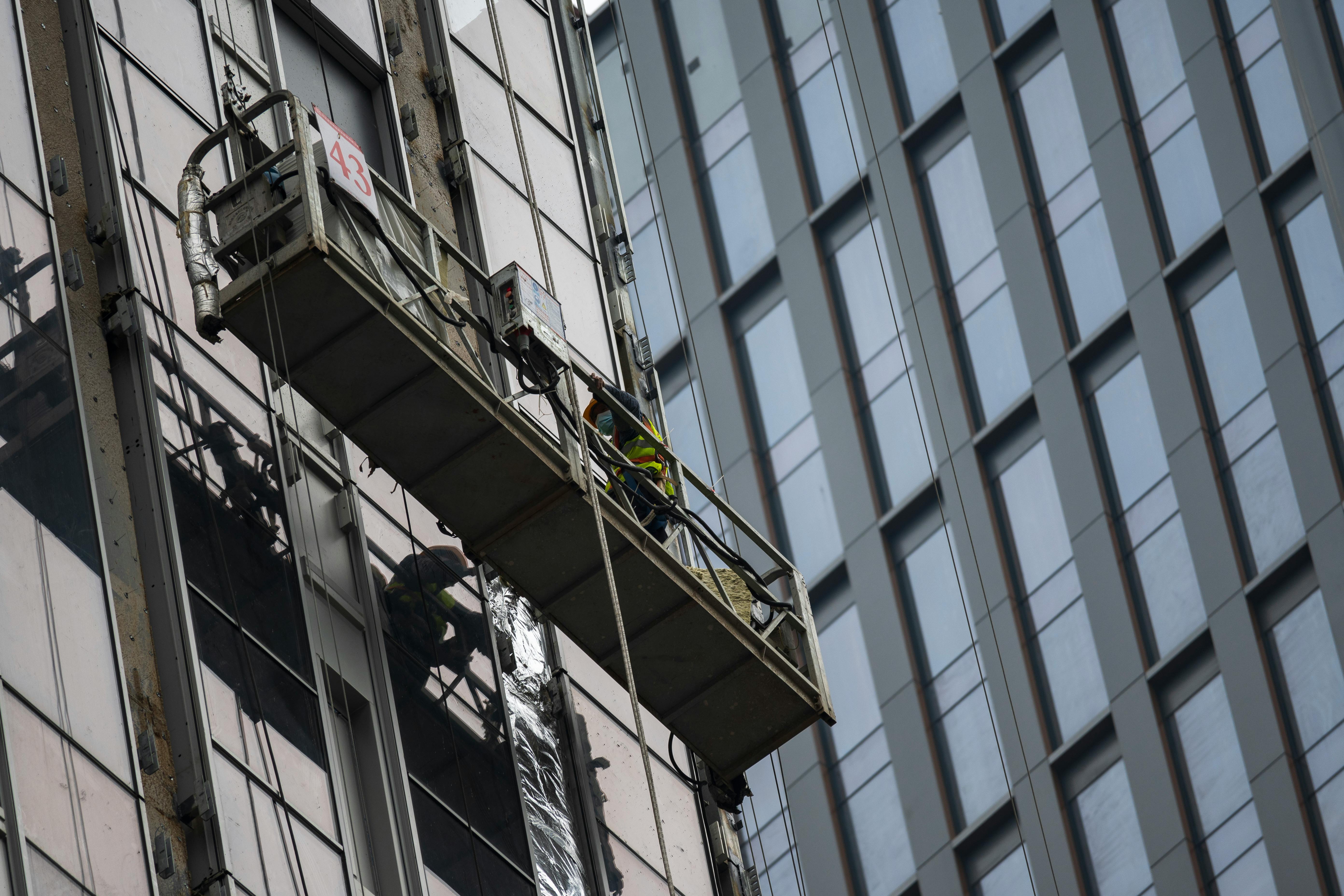 Gratis Trabajadores en una plataforma suspendida limpiando ventanas de un edificio alto en un paisaje urbano. Foto de stock