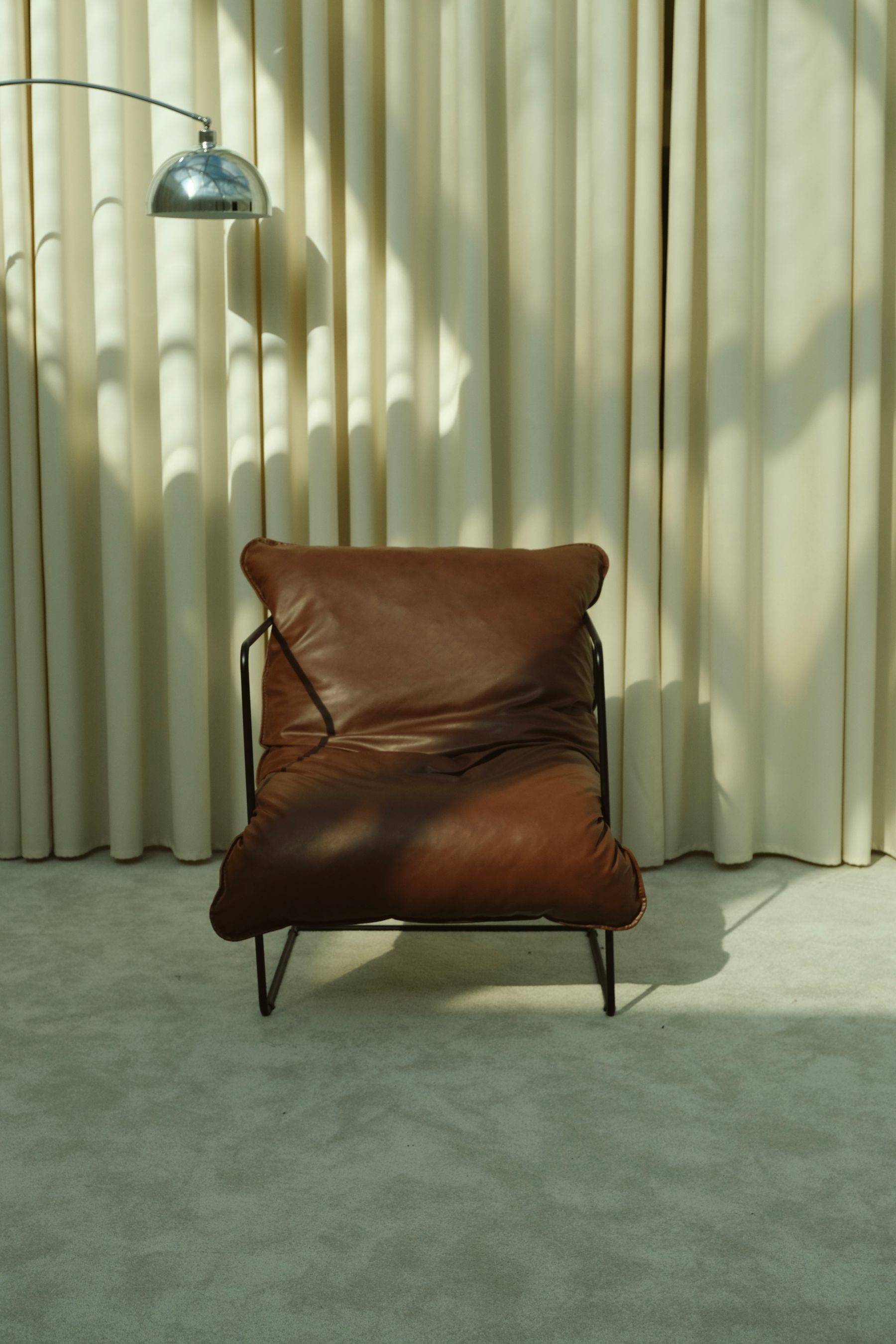 Retro arched metal floor lamp extending over a brown leather chair