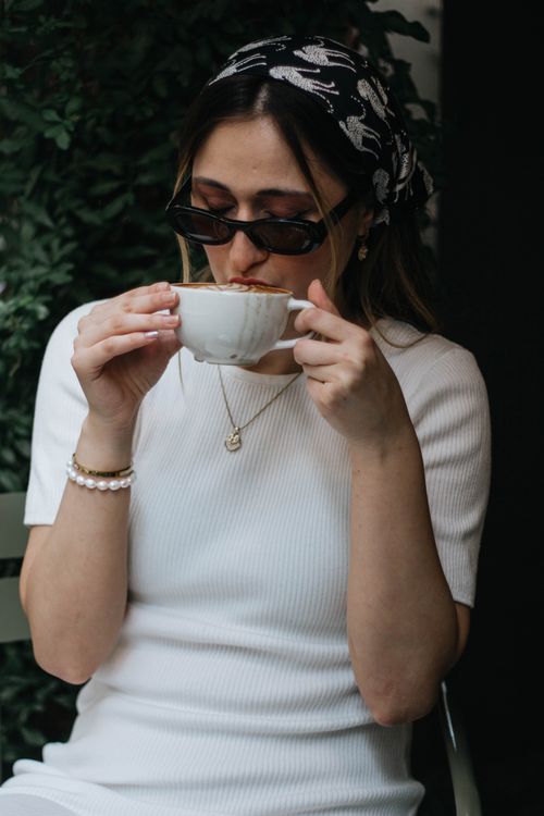 Free A fashionable woman enjoys coffee in an outdoor café setting, exuding a relaxed and chic vibe. Stock Photo