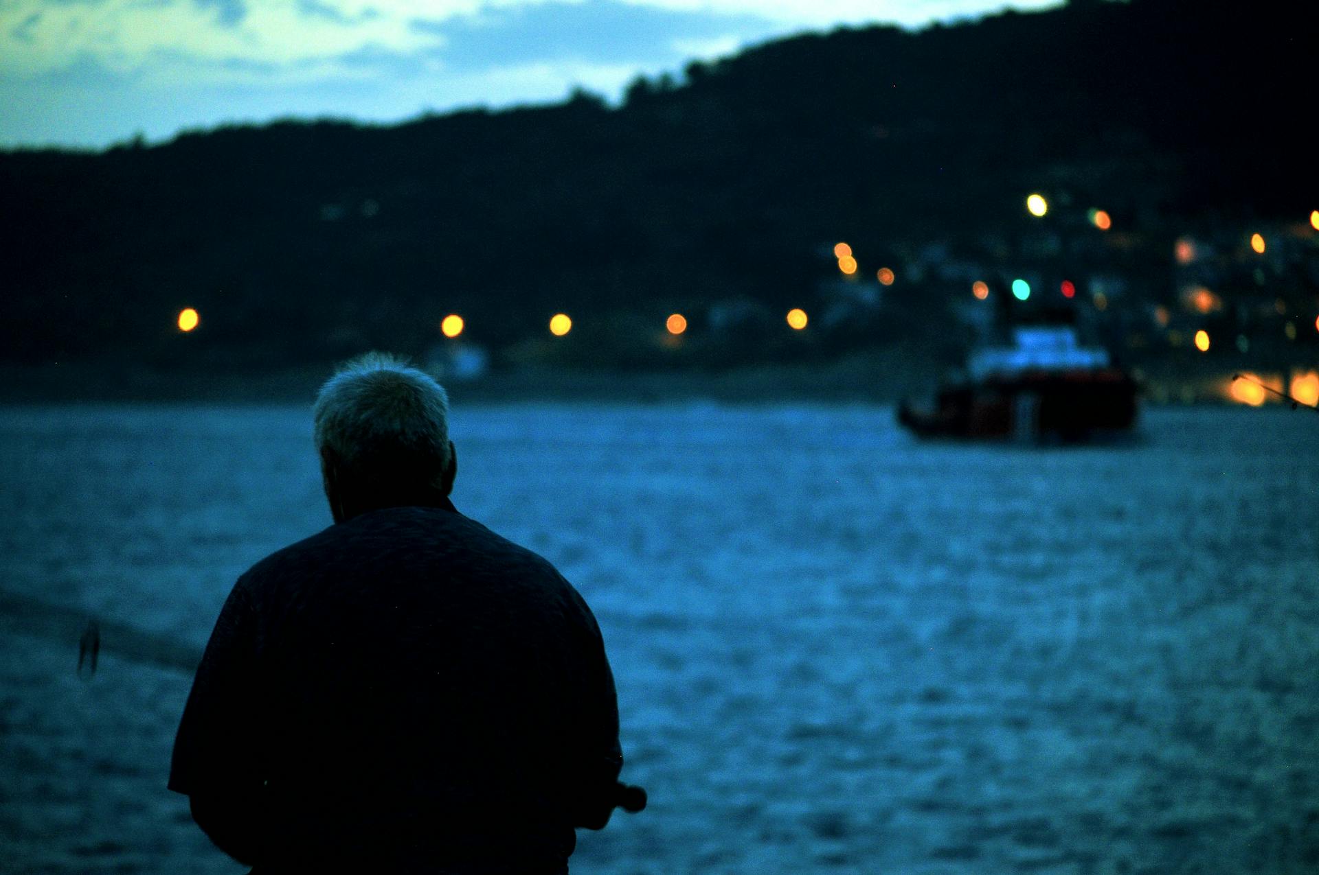 An elderly man fishes by the sea at dusk in Çanakkale, Türkiye, capturing the peacefulness of retired life.