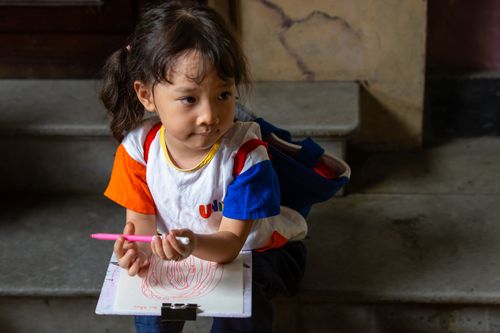 Free A young child sits indoors engaged in drawing with colored pencils, showcasing creativity and concentration. Stock Photo