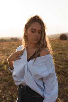 A young woman poses thoughtfully in a field during sunset, wearing a striped shirt.
