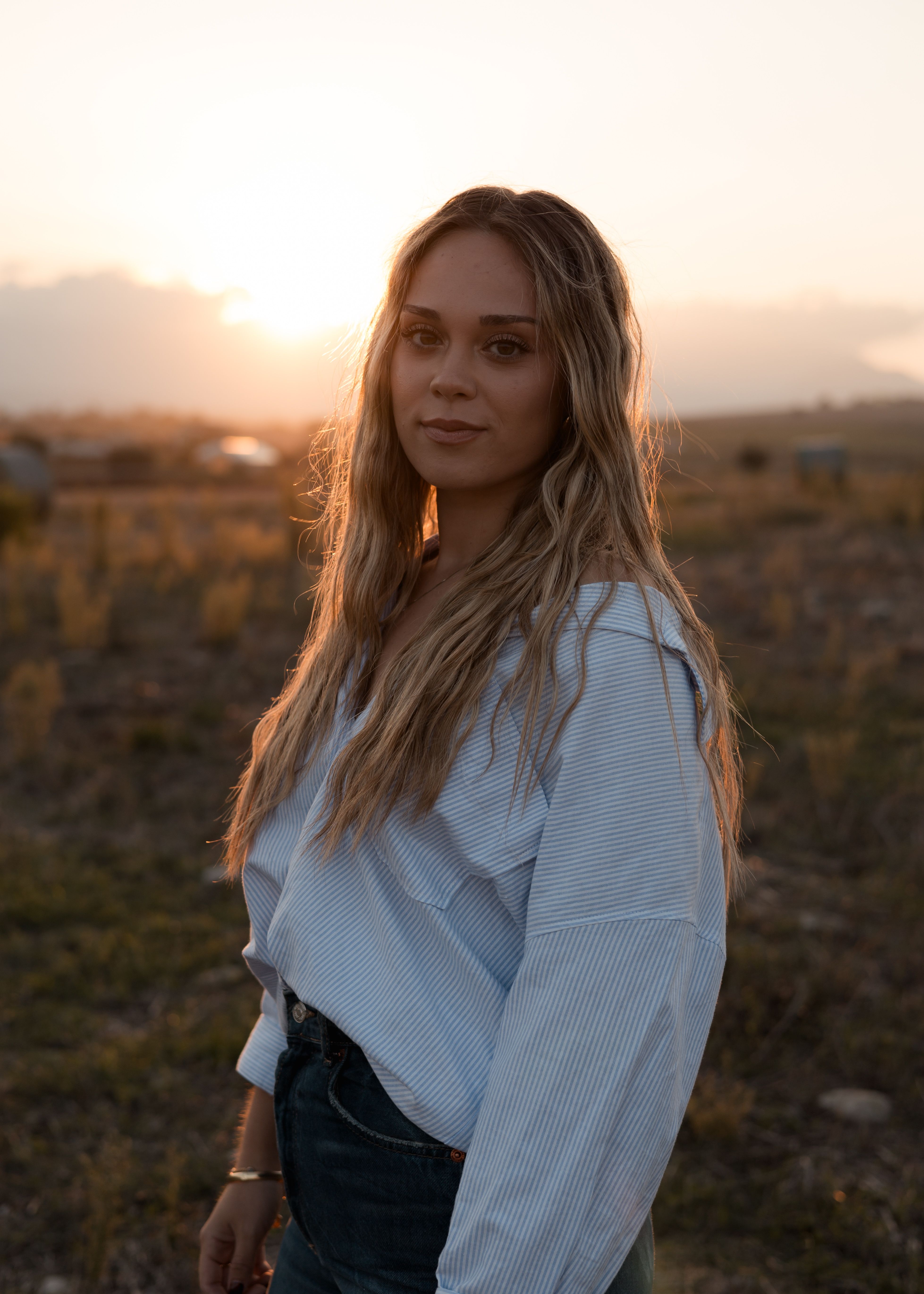 Young woman standing in a field at sunset, capturing natural beauty and serenity.