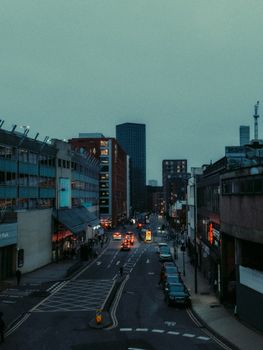 Urban street scene at dusk with illuminated city lights and cars on road.