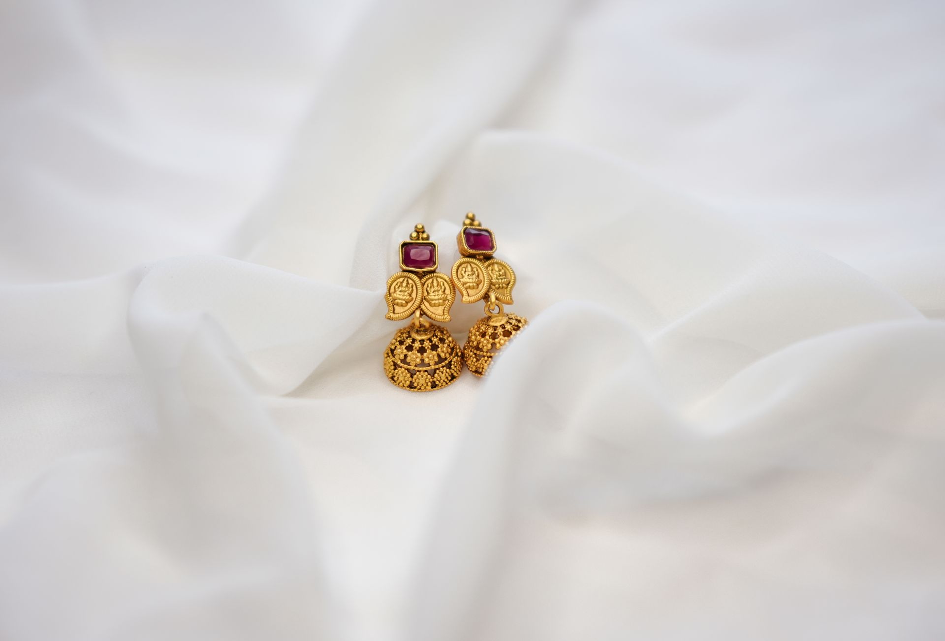 Elegant gold jhumka earrings with ruby accents displayed on white fabric, perfect for occasions.