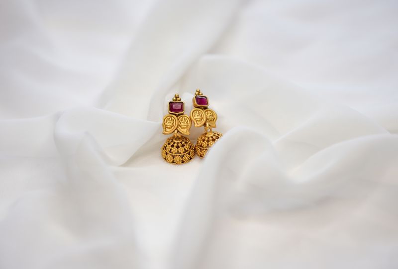 Elegant gold jhumka earrings with ruby accents displayed on white fabric