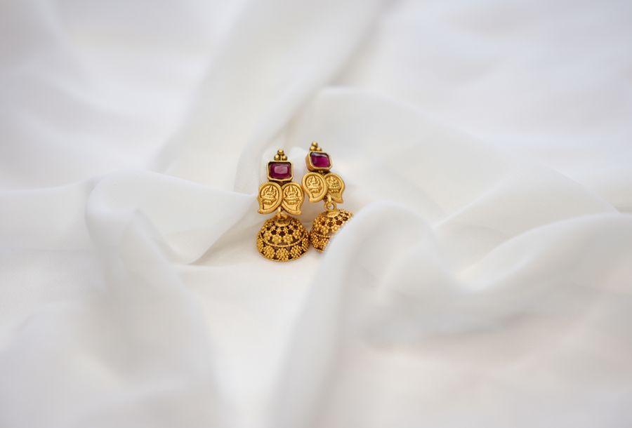 Pair of gold jhumka earrings with ruby-red accents laid on white fabric