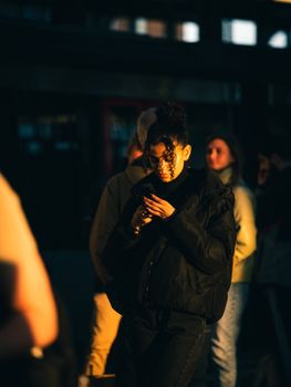 A young woman focused on her smartphone amidst a crowd in Amsterdam, highlighted by evening light.