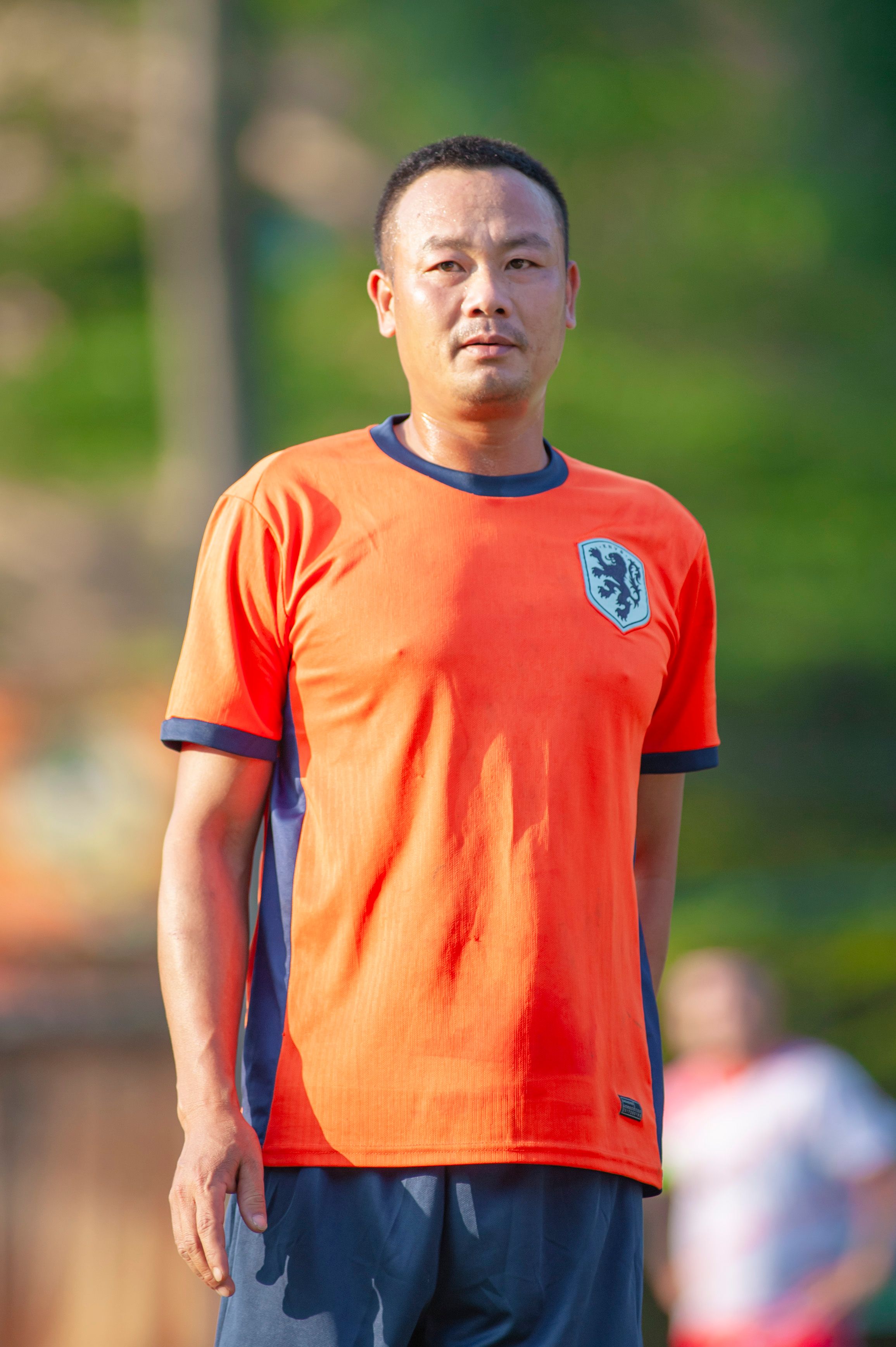 Outdoor portrait of a man in an orange sports jersey, green background.