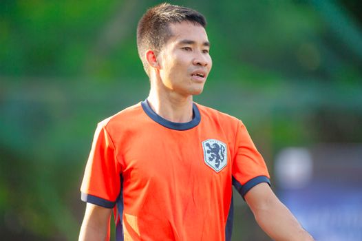 Male football player wearing an orange jersey during a game in Hà Nội.