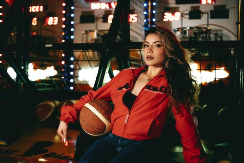 Free A fashionable young woman poses with a basketball in an arcade setting. Stock Photo