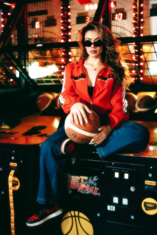 Free Stylish woman in red jacket posing with basketball in a vibrant arcade setting. Stock Photo