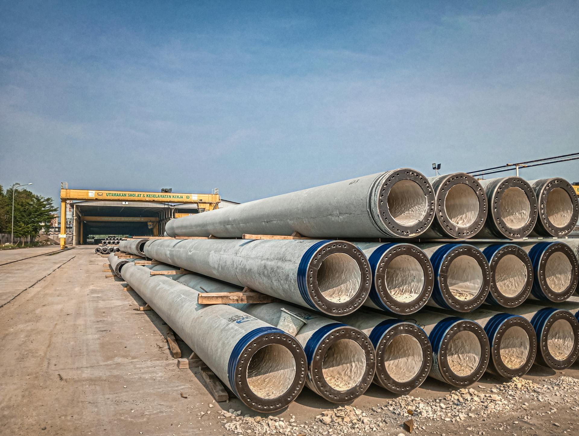 Stacked industrial concrete pipes near a construction area under clear skies.