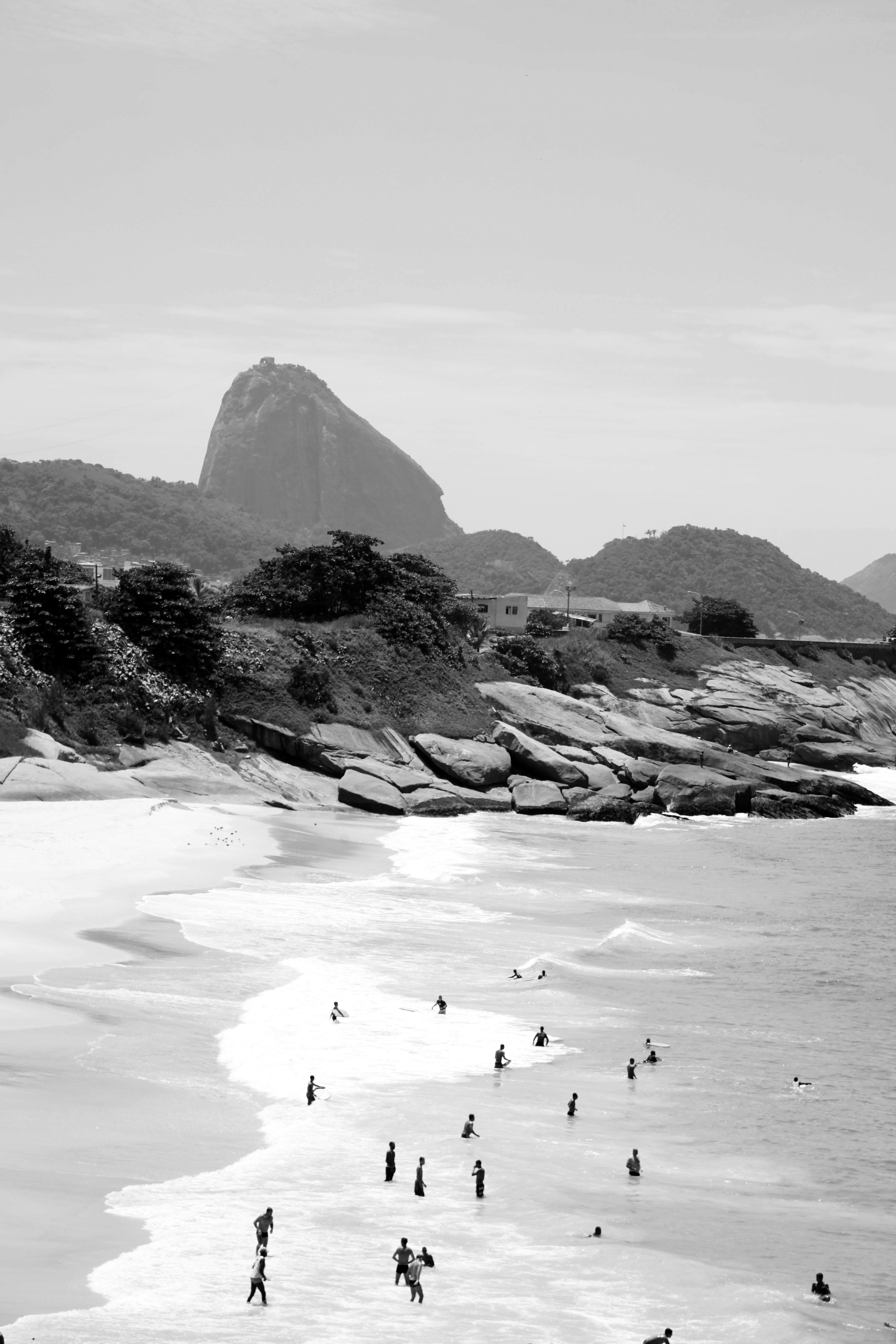 Black and white photo capturing Sugarloaf Mountain with people enjoying Rio beach.