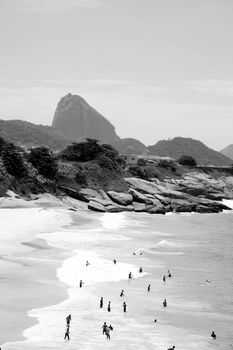 Black and white photo capturing Sugarloaf Mountain with people enjoying Rio beach.