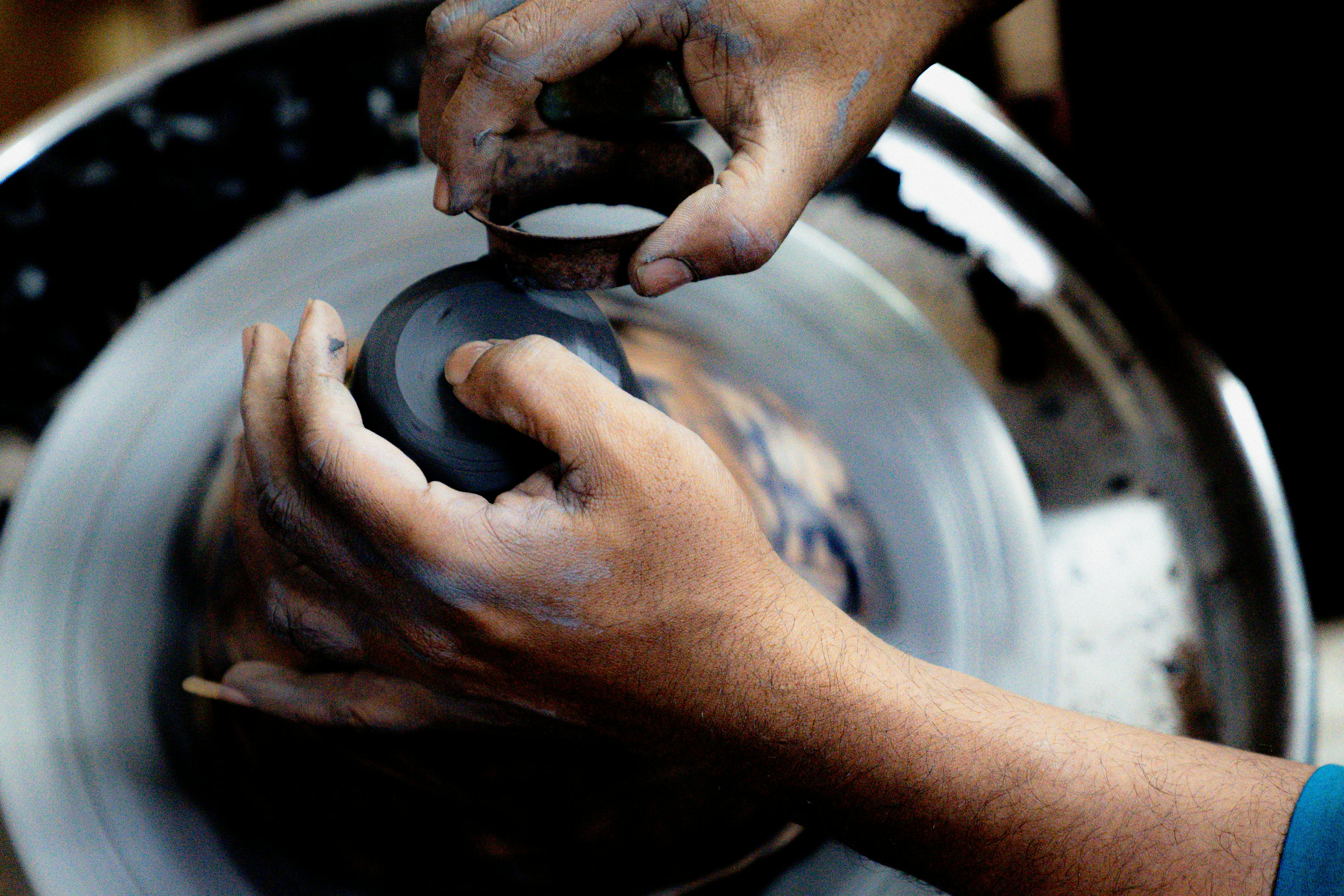 Artisan hands skillfully shaping clay pottery on a spinning wheel indoors.