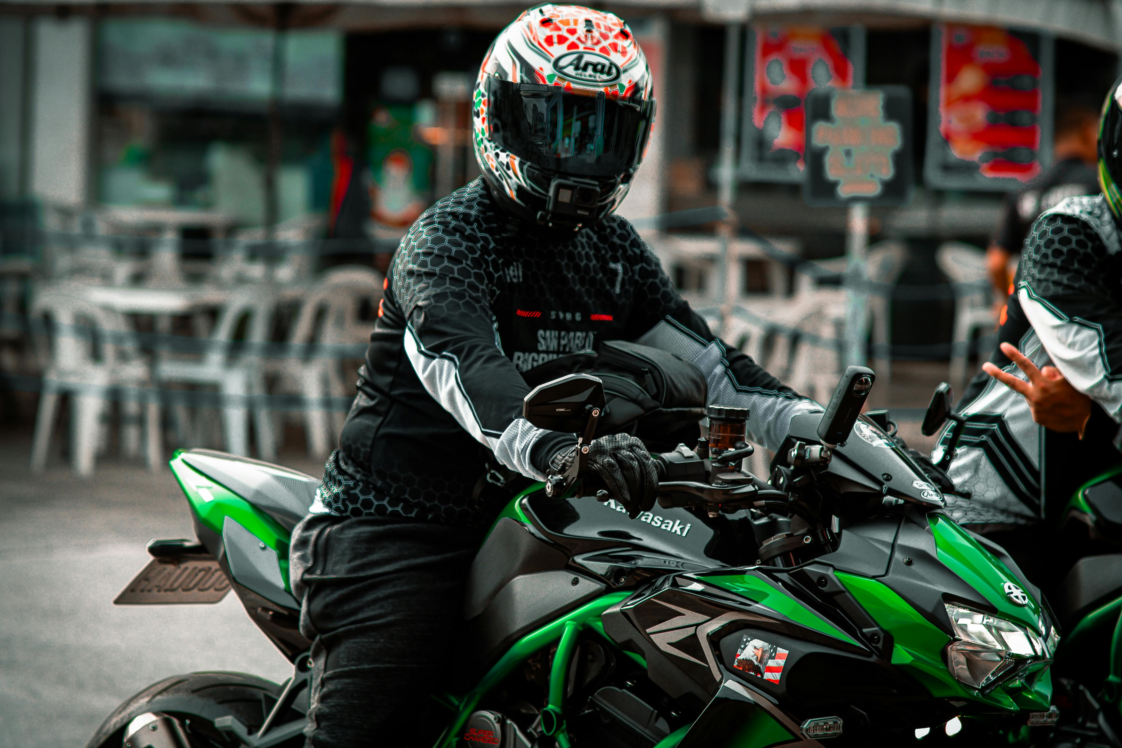 A motorcyclist in gear riding a green Kawasaki motorcycle in an urban setting.