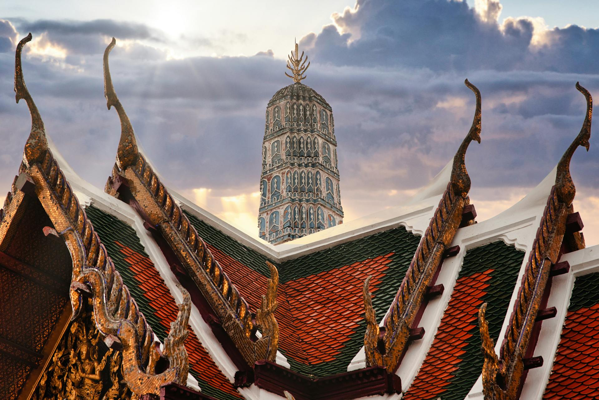 Intricate Thai roofs with Wat Arun in the background during a vibrant sunset in Bangkok.