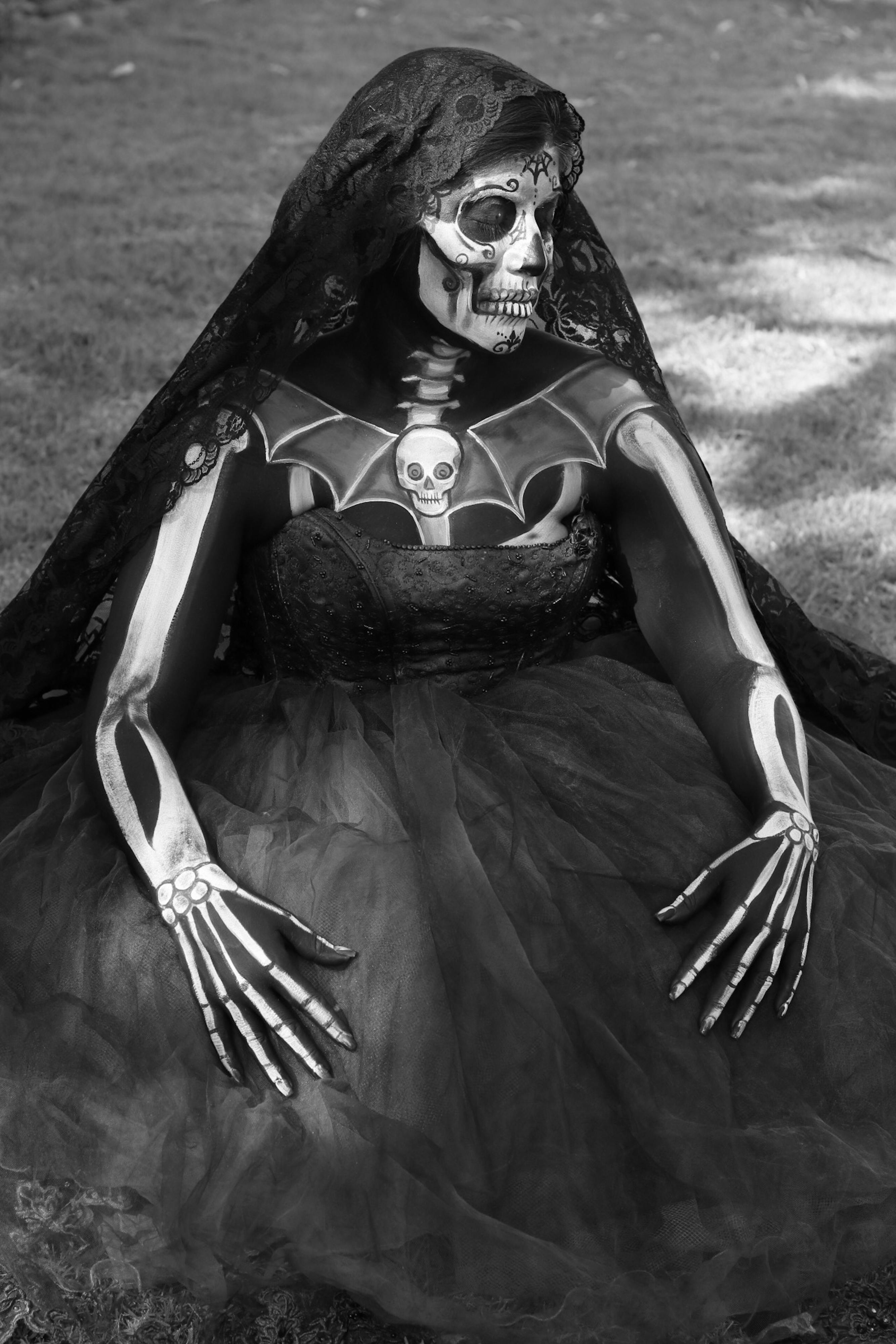 Ücretsiz Gotik iskelet makyajlı ve duvaklı bir kadın dışarıda çimlerin üzerinde oturuyor. Stok Fotoğraflar