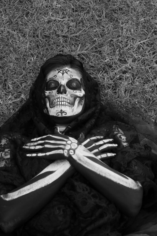 Free A person with intricate Day of the Dead skeleton makeup lying on grass wearing a lace shawl. Stock Photo