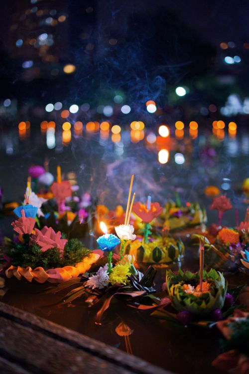 Free Colorful krathongs float on water during Bangkok's Loi Krathong festival, lit by candlelight at night. Stock Photo