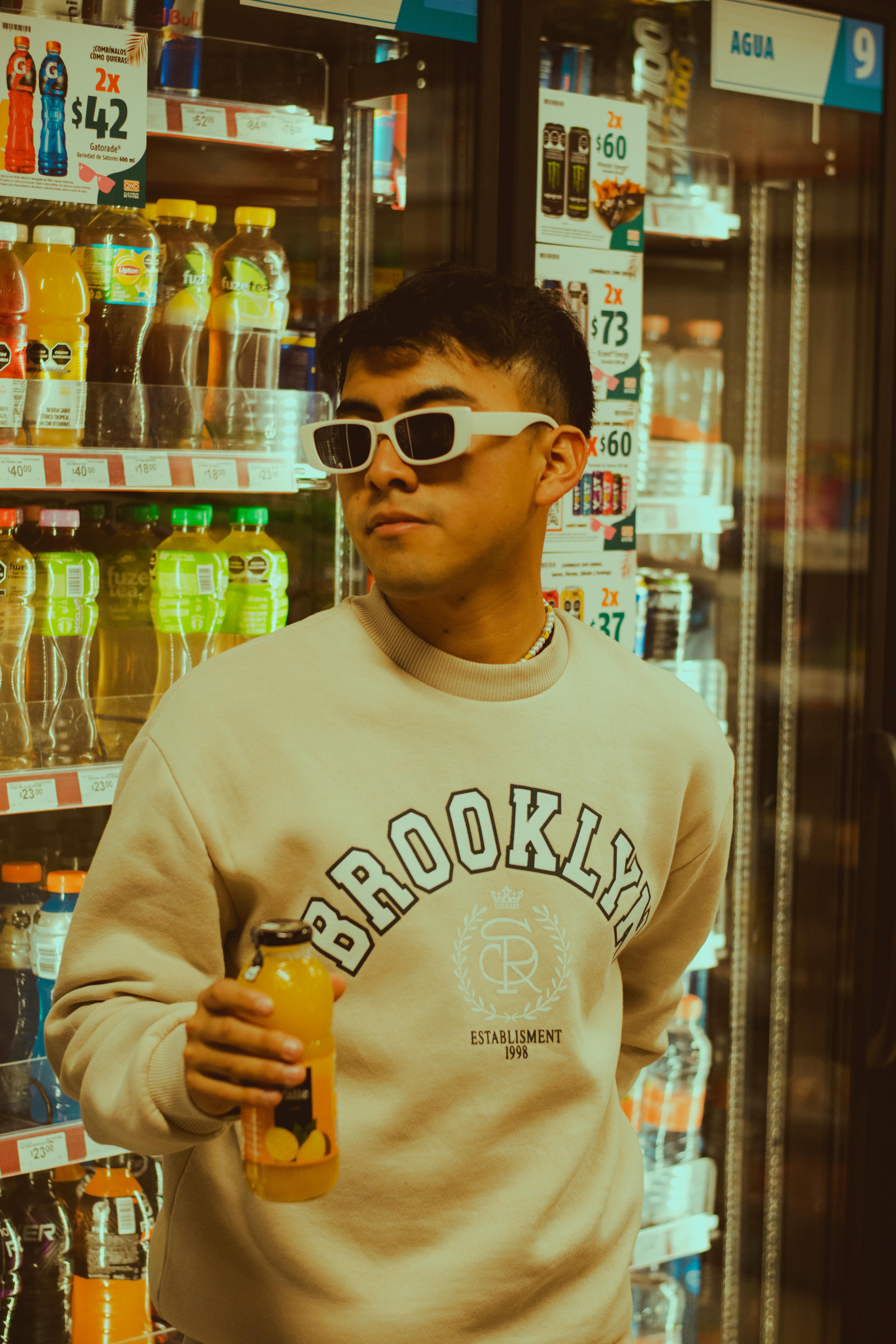 Stylish young man with sunglasses holding a juice in a store aisle.