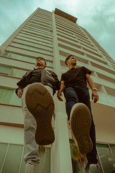 Low-angle view of two men standing against a tall building, showcasing urban style.