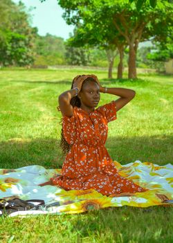 A young woman sits on a picnic blanket outdoors, enjoying a sunny day.