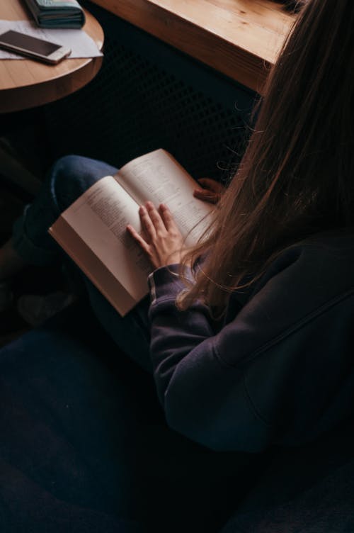 無料 本を読みながら椅子に座っている黒いジャケットを着ている女性 写真素材