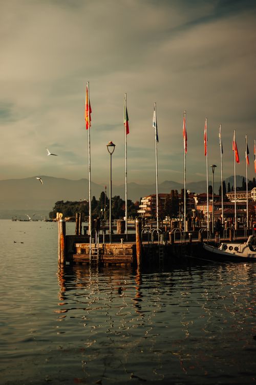 Free A serene waterfront view with flags fluttering over a dock in Italy. Stock Photo