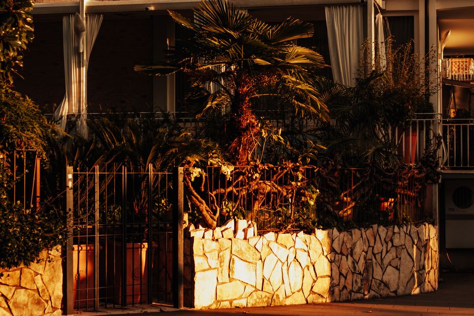 A beautiful sunset casts a warm glow over a garden with lush foliage and stone wall, creating a peaceful ambiance.