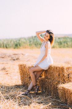 Serene outdoor portrait of a woman sitting on a hay bale in a sunny rural field.
