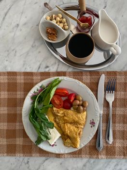 A healthy breakfast featuring an omelette with fresh greens and coffee on a marble table.