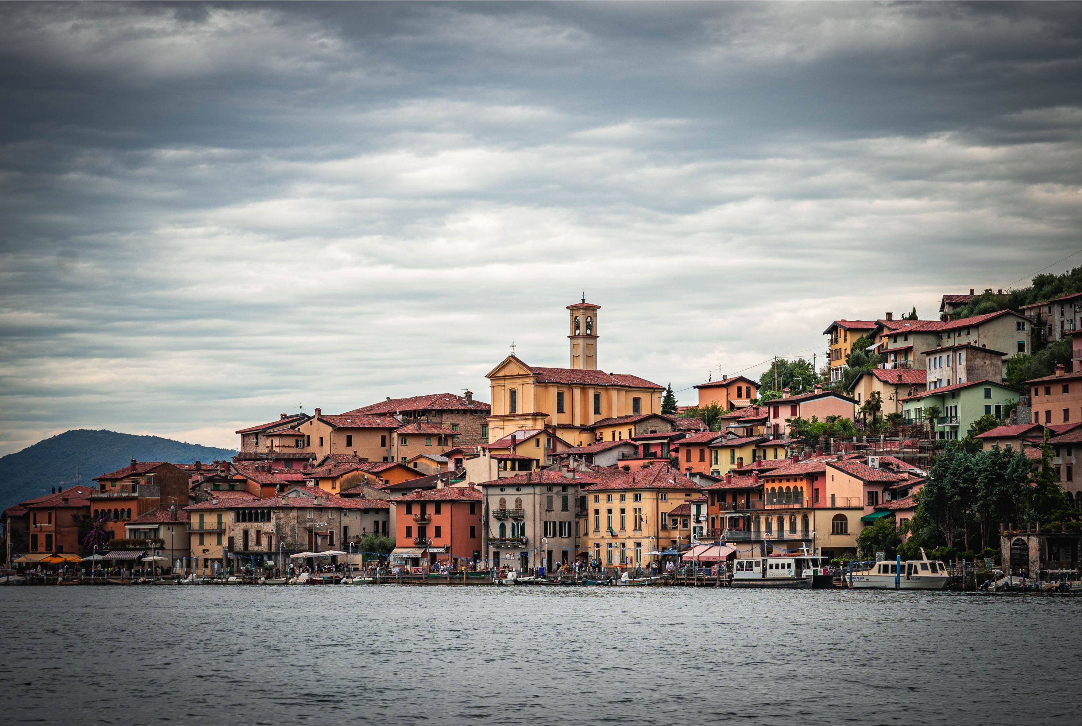 Picturesque Italian village by the lake under cloudy skies, showcasing vibrant architecture.
