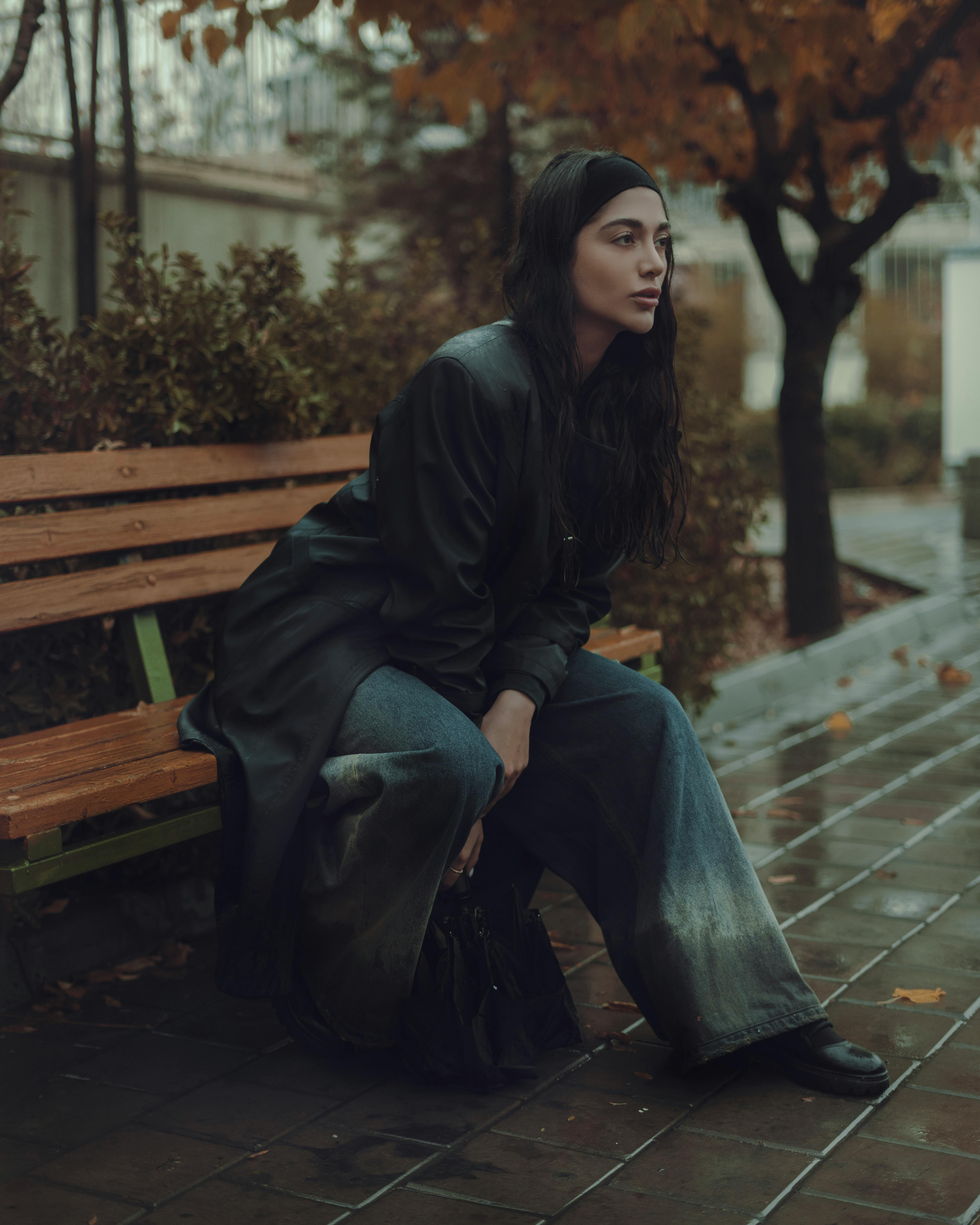 Young woman in stylish autumn clothing sitting on a bench in a quiet park setting.