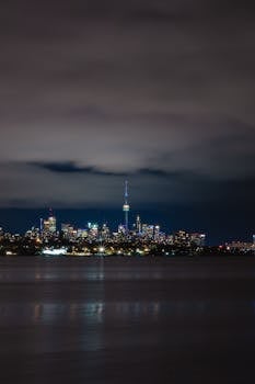Nighttime Toronto skyline featuring CN Tower over Lake Ontario with city lights.