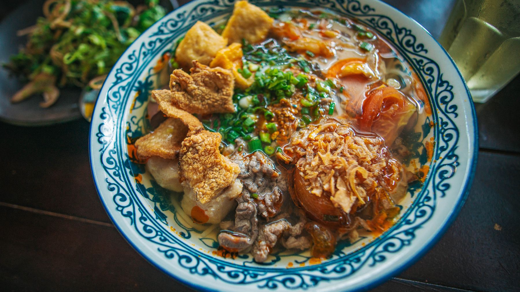 Eine dampfende Schüssel vietnamesischer Pho, garniert mit Kräutern und knusprigen Toppings.