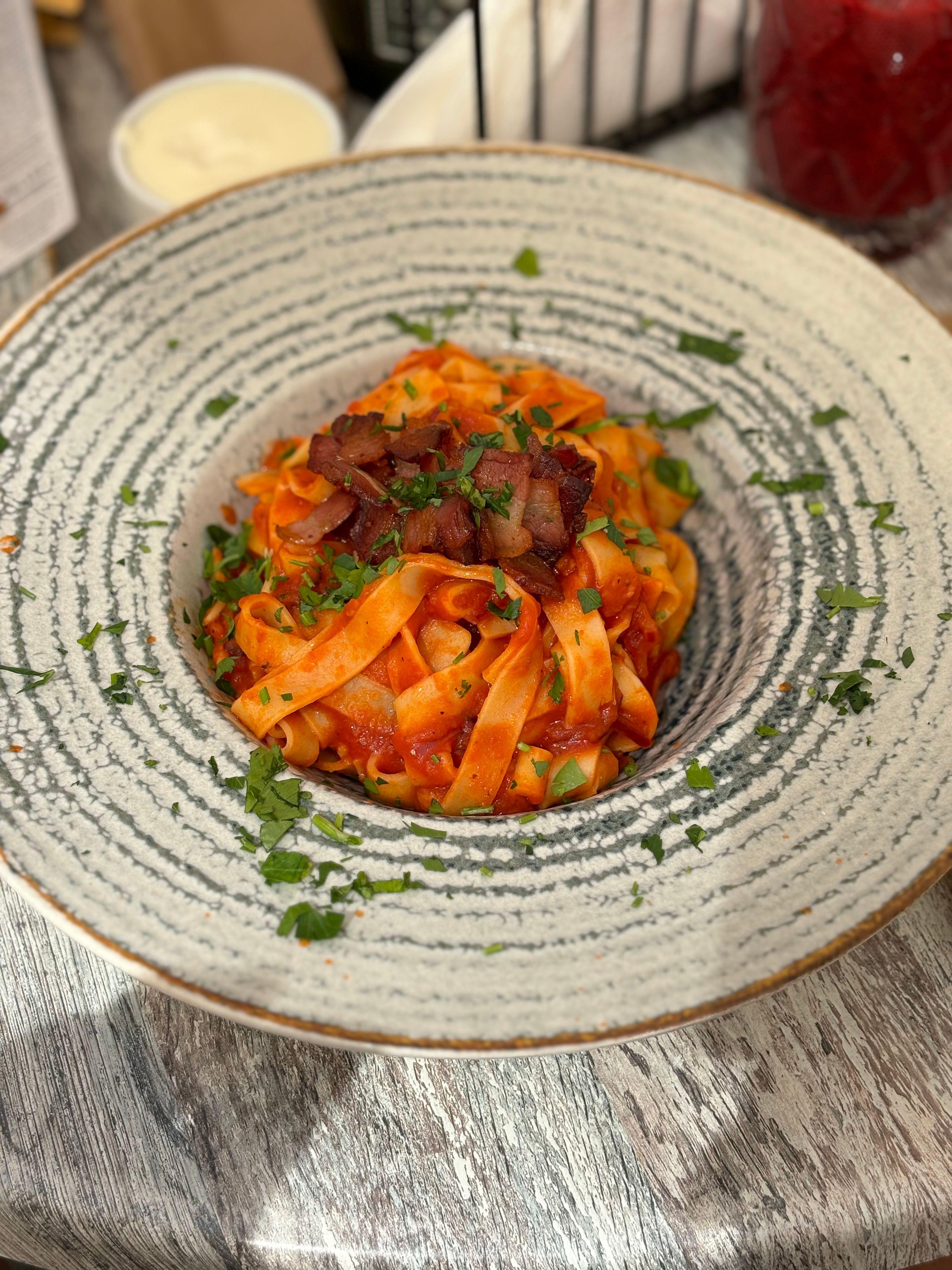 Savor a bowl of tagliatelle with rich tomato sauce and crispy bacon.