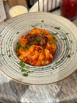 Savor a bowl of tagliatelle with rich tomato sauce and crispy bacon.