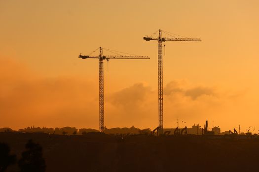 Silhouette of tall construction cranes against a vivid sunset sky, capturing urban development.