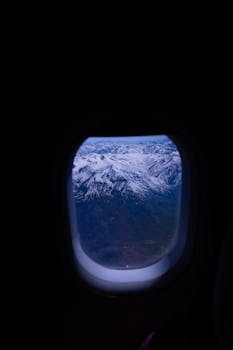 Aerial view of the snow-covered Andes through an airplane window during flight.