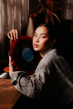 在灯光温暖的室内，一位时尚的年轻女子手持黑胶唱片，散发着复古的气息