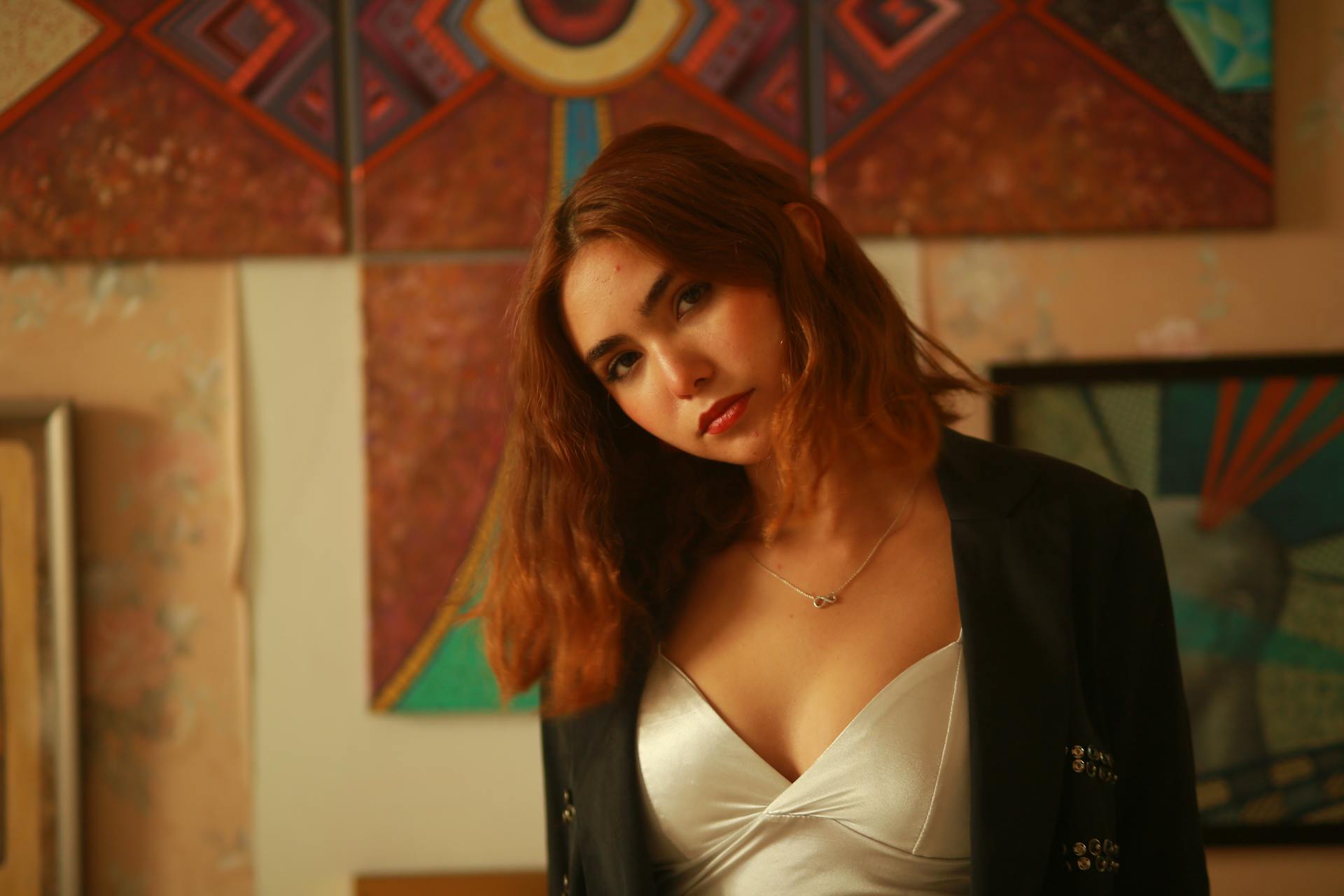 Portrait of a woman in a silver dress and blazer, set against an artistic and warm-lit interior.