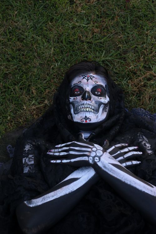 Free Close-up of person with intricate skeleton makeup lying on grass, Halloween theme. Stock Photo