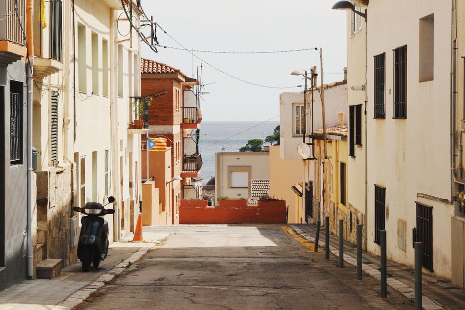 Calle tranquila en un pueblo mediterráneo que conduce al mar bajo un cielo despejado.